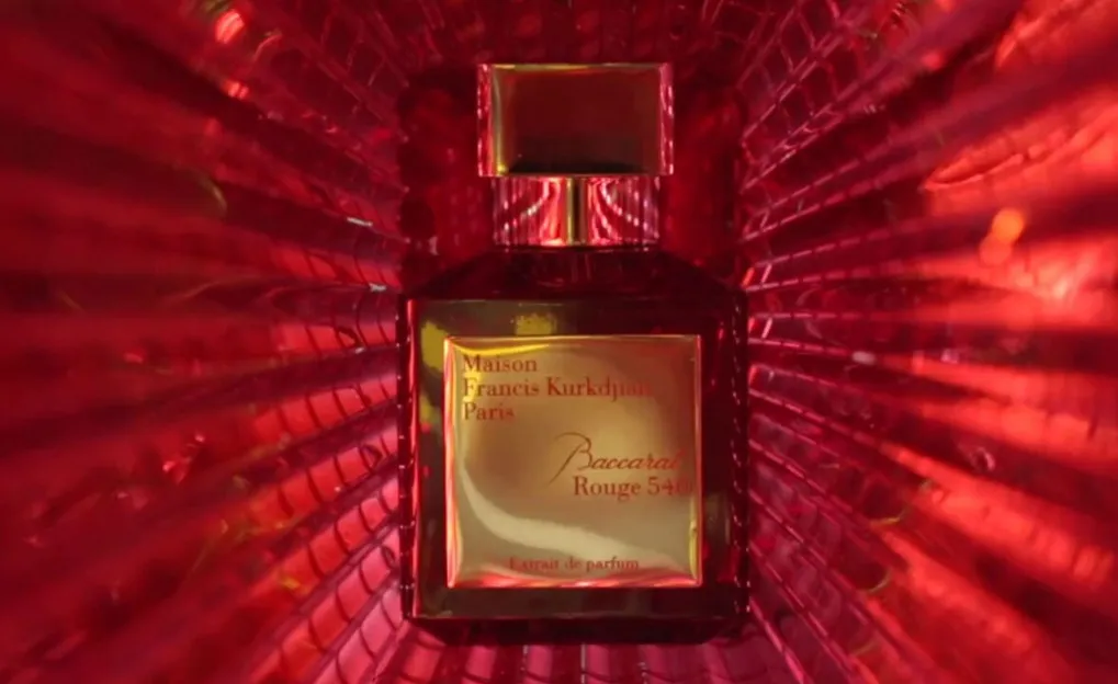 Frasco do perfume Baccarat Rouge 540 da Maison Francis Kurkdjian em tom vermelho intenso, com fundo iluminado em padrão radial vermelho, transmitindo luxo, intensidade e sofisticação.