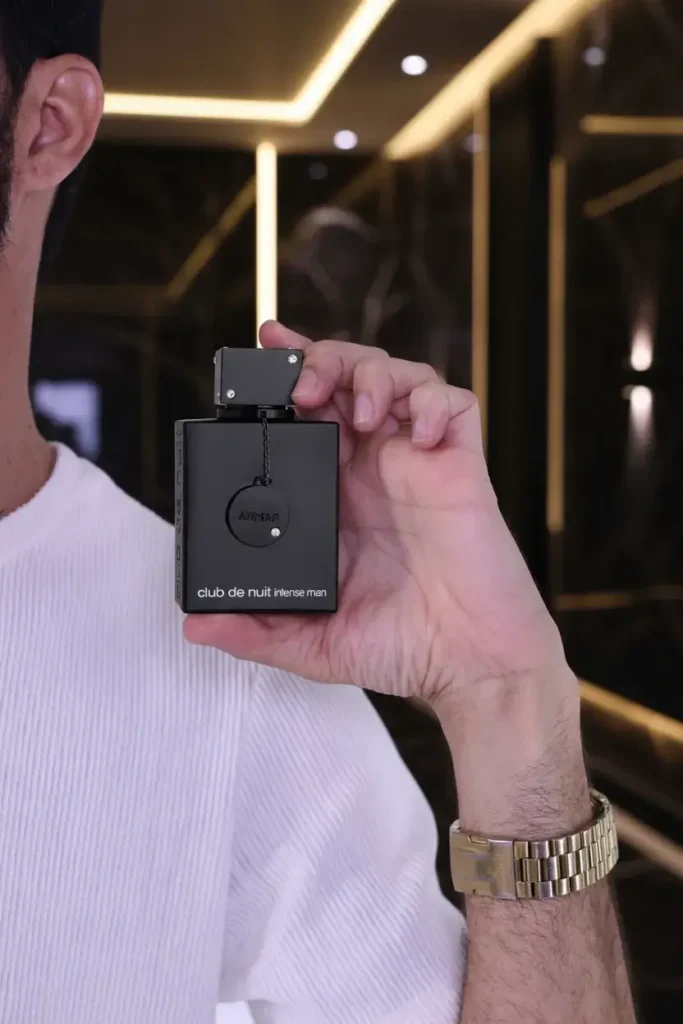 Homem segurando perfume Club de Nuit Intense Man em ambiente moderno, representando fragrância marcante, intensa e de alta fixação