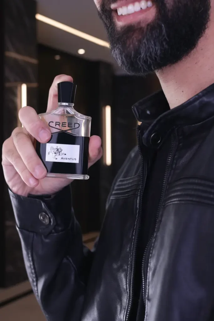 Homem elegante segurando perfume Creed Aventus em ambiente moderno, representando fragrância sofisticada, masculina e de alto padrão